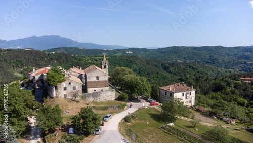 Aerial view of the ancient stone buildings and church of Hum nestled amid the vibrant green hills, a timeless scene under a clear sky, Hum, Istria County, Croatia.