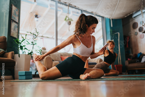 Photos A woman in a white sports bra and black shorts stretches on a yoga mat while another participant sits in the background