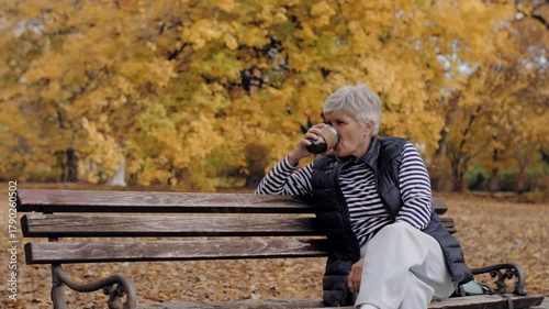 Senior woman drinking coffee on park bench during autumn