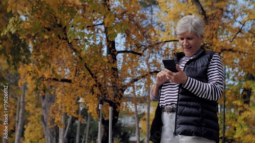 Mature woman with luggage using smartphone in autumn park