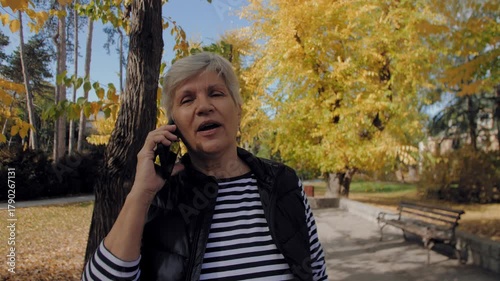Senior woman walking and talking on a smartphone in an autumn park