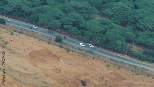 A cinematic shot of a road near Pushkar showing desert on one side and lush greenery on the other, with cars moving in the frame. 