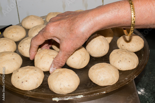 woman’s hand placing sattu filled dough balls on grass tray for baking or cooking purpose. Litti or bati. step or process of making litti