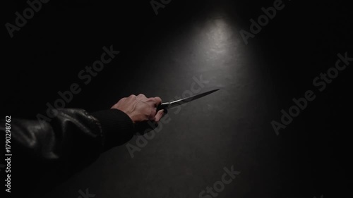 POV, close-up first person view of a man's hand with big knife. Criminal hand holding kitchen knife in threatening posture on dark background, causes alarm and danger.