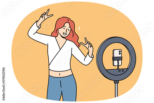 Woman blogger dances in front of phone on tripod with ring lamp, ready-made video for social networks. Video blogger girl smiles while broadcasting live for subscribers and fans from internet.