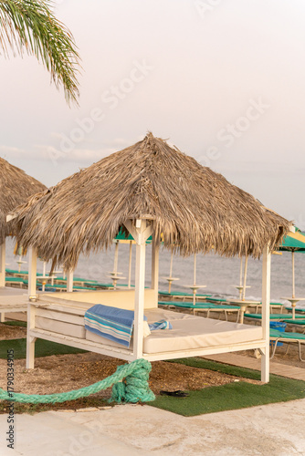 A beachside cabana is arranged with a comfortable bed and towels. This serene setting offers a perfect spot to unwind by the calm sea at sunset.