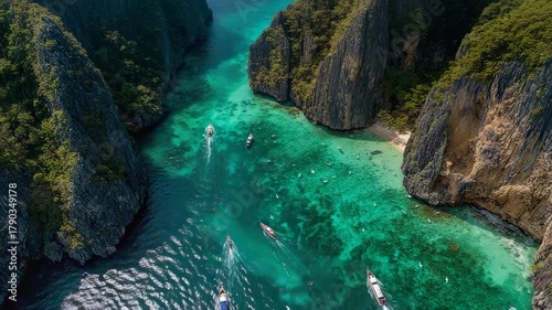 Aerial view of turquoise bay surrounded by towering cliffs with colorful boats gliding over clear water, waves brushing the sand and birds flying overhead. Perfect for travel and nature videos.