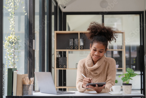 Young African American businesswoman working at a desk and using a digital tablet in the modern office.
