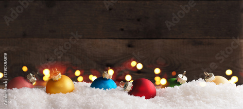 Colorful vintage Christmas baubles in snow on a wooden background with Christmas lights, holiday or seasonal backdrop