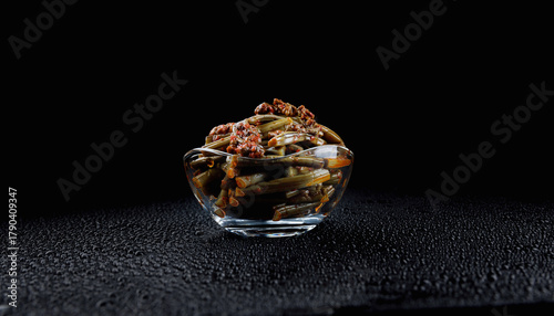 Konstfotografi A glass cup with bracken fern salad with spices stands on a beautiful black background with water drops
