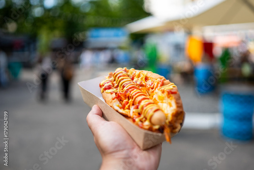 Quadro em tela A close-up, point-of-view shot of a hand holding a delicious hot dog topped with