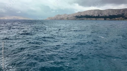 Dynamic coastal waves under cloudy sky with mountainous horizon