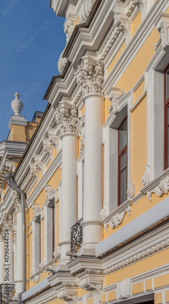 Fototapeta premium Facade fragment of an old mansion in an eclectic style with rich stucco moldings and columns. An elegant architectural background for the concept of luxury, culture, and history.