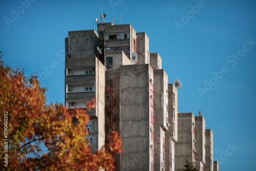 Residential brutalist building in New Belgrade with balconies framed by trees against a clear blue sky.