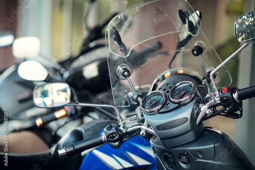 Close-up of a scooter's dashboard, speedometer, mirrors, and transparent windshield.