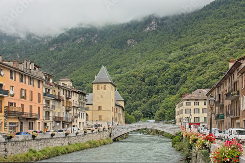 historical bridge and tower along Isere river with mountain with forest behind in the city of Moutiers, Savoie, France 