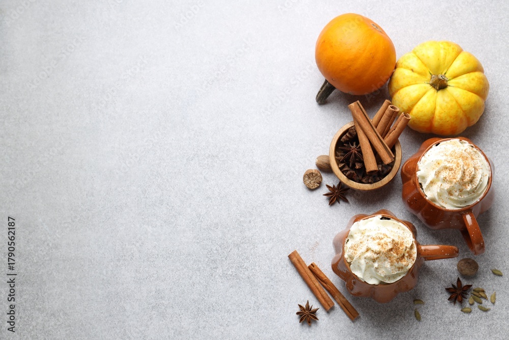 Fototapeta premium Tasty pumpkin latte with whipped cream in cups, spices and ingredients on light grey table, flat lay. Space for text