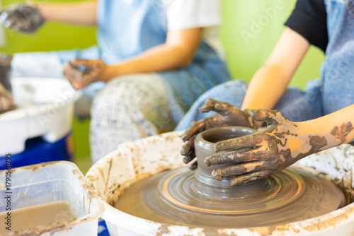 Close up of child hands shaping clay on pottery wheel in selective focus during workshop. Learning pottery, creative education, handmade ceramic art, artisan craft, and childhood skill.