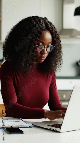 Focused african american woman reviews documents while working on laptop at home office