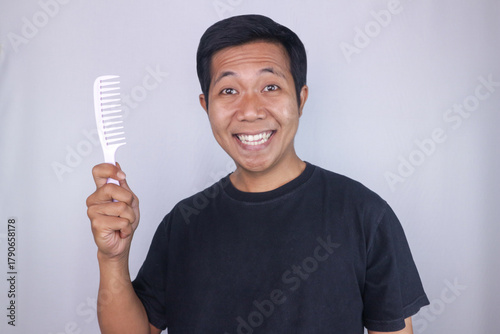smiling asian man holding comb, isolated on white background. Hair care concept