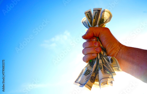 Dollars in hand on blue sky. Crumpled pile of dollar bills in male hand on sky,  space for text. Person clutching handful of crumpled dollar bills tightly. Crumpled Money in hand. Crumpled money US.