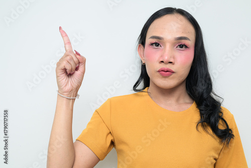 Fototapeta Portrait of a young Thai transgender person against white background pointing fi