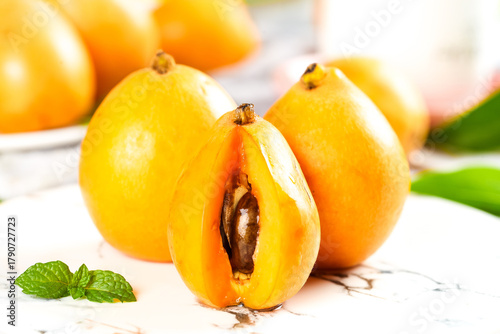 Fotografie Fresh Ripe Loquat Fruits Cut in Half Showing Seed on White Marble Surface with M