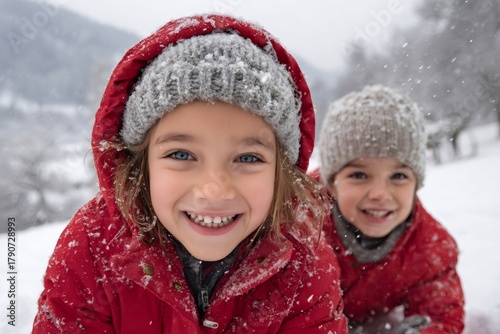 Two smiling children wearing red coats playing in the snow