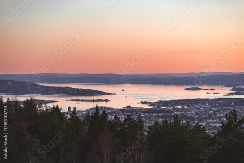 Photography Soft pastel sunset over Oslofjord with islands, calm water and forested hills, r