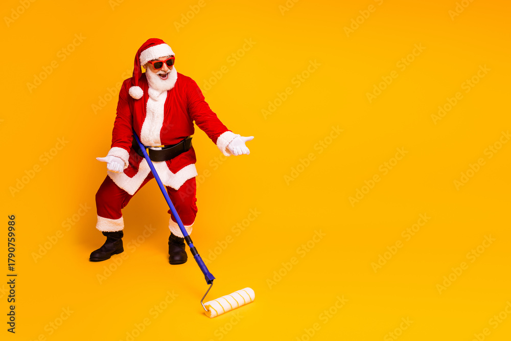 Fototapeta premium Santa in a red costume with a paint roller yellow backdrop ready for festive home improvement humor and Christmas marketing campaigns