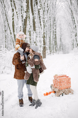 Young family with two children standing in winter forest and posing for a photo
