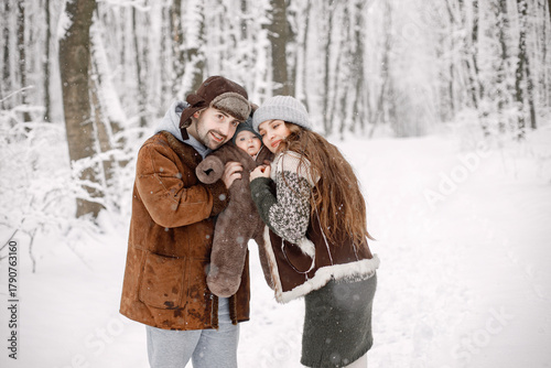 Young family with baby son on hands standing in winter forest