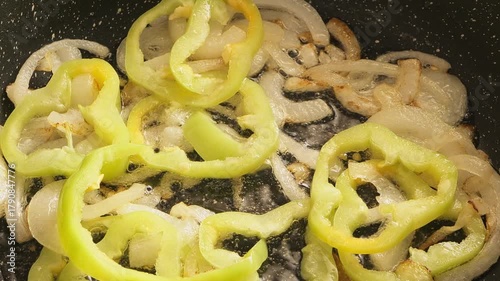 White onion rings and yellow bell peppers fried in a pan with olive oil