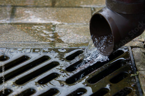 Photos Rainwater drainage pipe flowing into metal grate outdoors