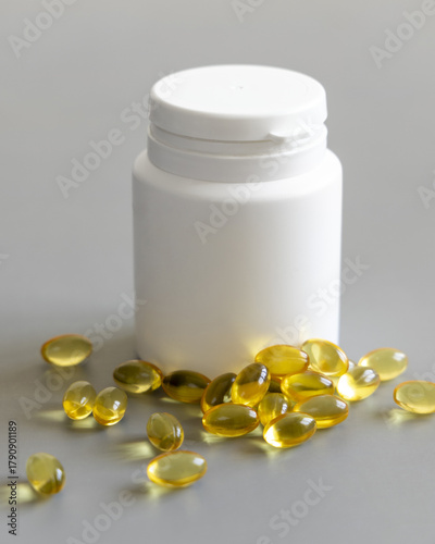 Yellow softgels (gelatin capsules) and bottle on a grey close up, mockup. Omega 3 Fish oil or garlic oil