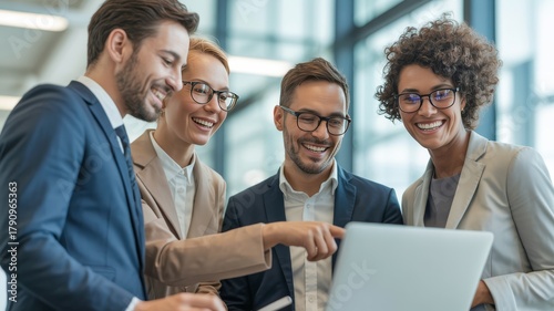 Diverse Business Team Celebrating Success in Modern Office. diverse group of four smiling business professionals standing. They are collaborating around a laptop, one person is pointing at the screen