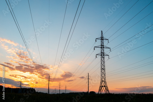 A tall power tower with many wires is silhouetted against a beautiful sunset sky