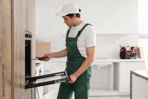 Photos Male worker with screwdriver installing built-in oven in kitchen