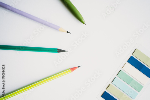 Minimalist flat lay of a blank white page, surrounded by colorful pencils, a pen, and pastel sticky notes, representing creativity, planning, and starting new projects