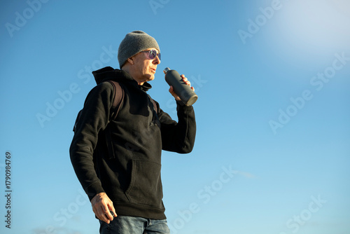 male hiker drinking water from a bottle, outdoors winter sun