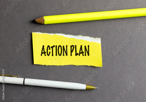  Words action plan on yellow torn paper with pencil and pen on dark background