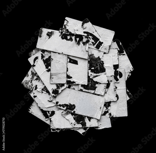 Pile of old torn paper stickers with worn textures and black-and-white print remnants, arranged on a solid black background.