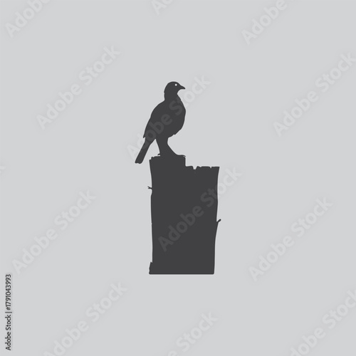 a solitary bird perched atop a dark weathered stone structure against a muted gray backdrop