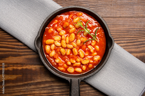Baked bean dish in cast iron pan on wooden background.