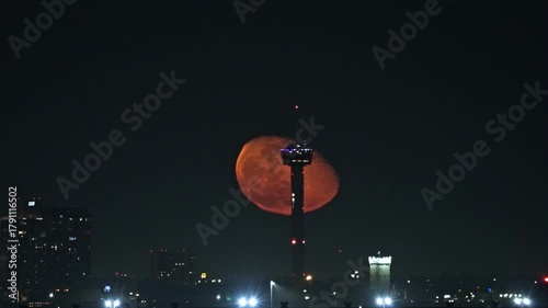 Vibrant Moon Rising Behind the Tower of Americas as Elevator Descends. San Antonio City Skyline Night Scene.