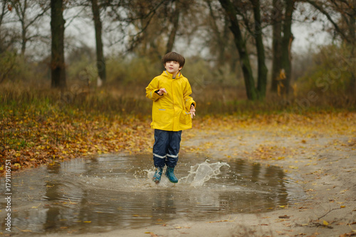 Happy child in a yellow raincoat jumping in puddles on a rainy autumn day in the park.