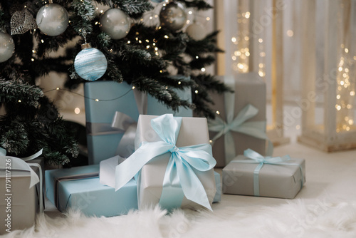Decorated Christmas trees with blue and silver baubles and wrapped gifts on white wooden floor. Concept of winter holidays, celebration, cozy home interior.