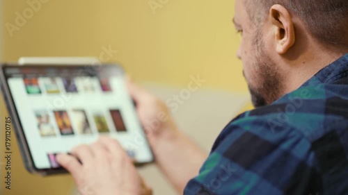 Man chooses film or Tv show to watch on an online steaming service app at home.
