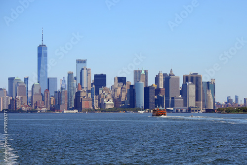 manhattan skyline and orange ferry boat navigating toward new york island