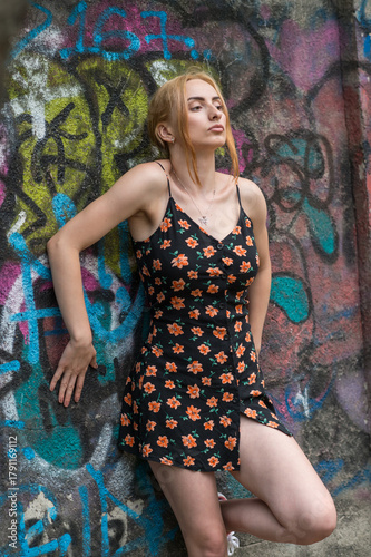 Blonde sensual woman with long legs posing confidently in front of a colorful graffiti wall, wearing a short floral dress. Urban fashion meets vibrant street art in this expressive portrait.